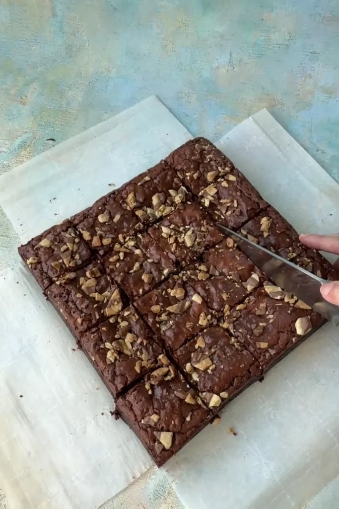 Knife cutting fudgy brownies into clean squares on parchment paper