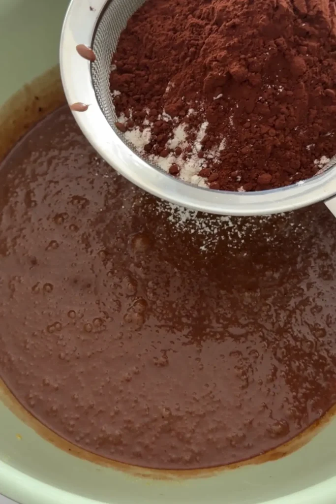 Sifting cocoa powder and flour into brownie batter