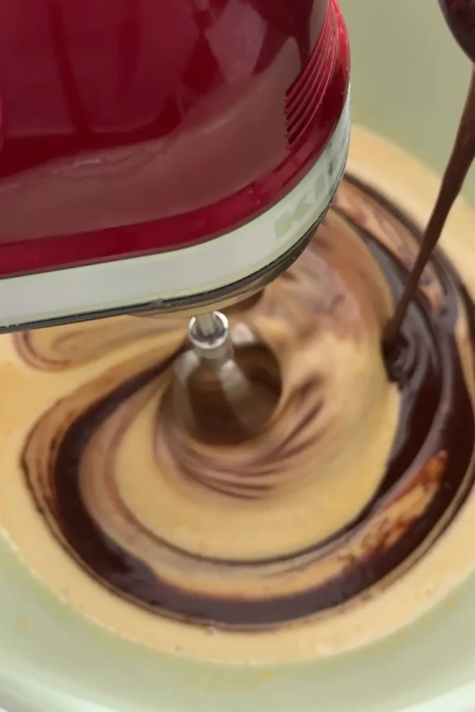 Pouring melted chocolate into whipped egg mixture to combine