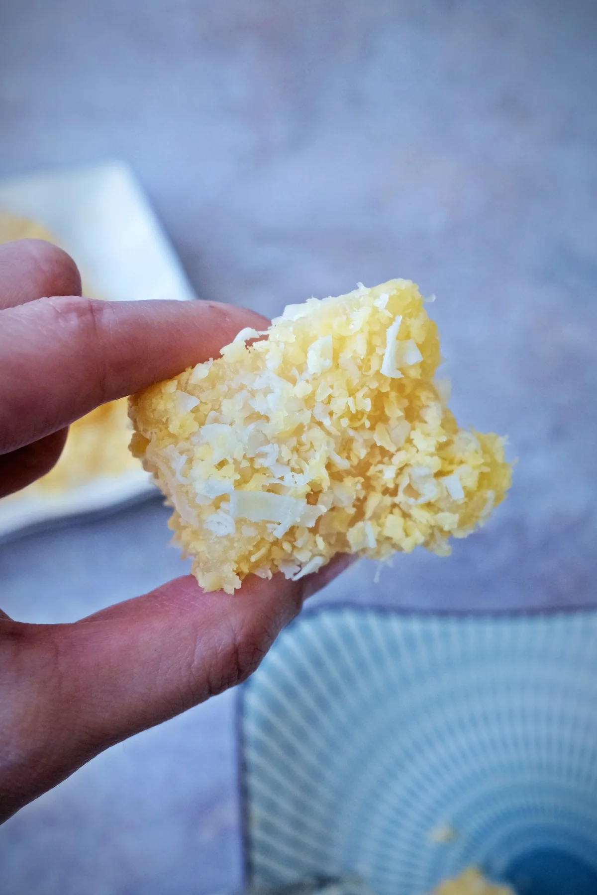 Hand holding a piece of pichi pichi cassava dessert coated in grated cheese