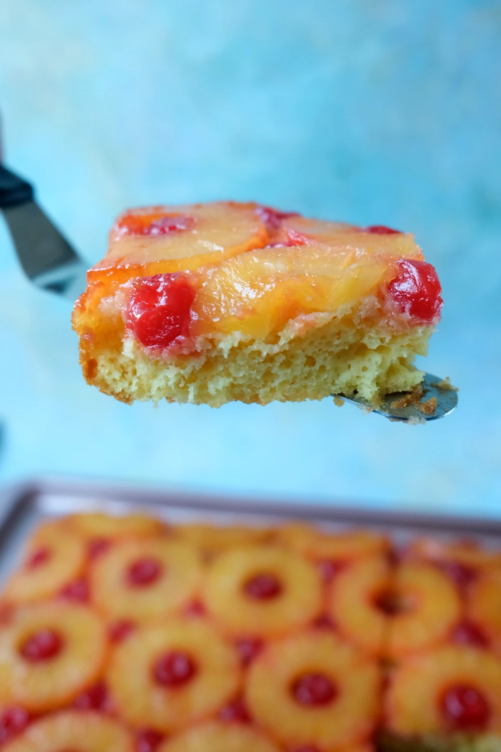 Slice of pineapple upside down cake lifted from the pan with pineapple and cherries on top