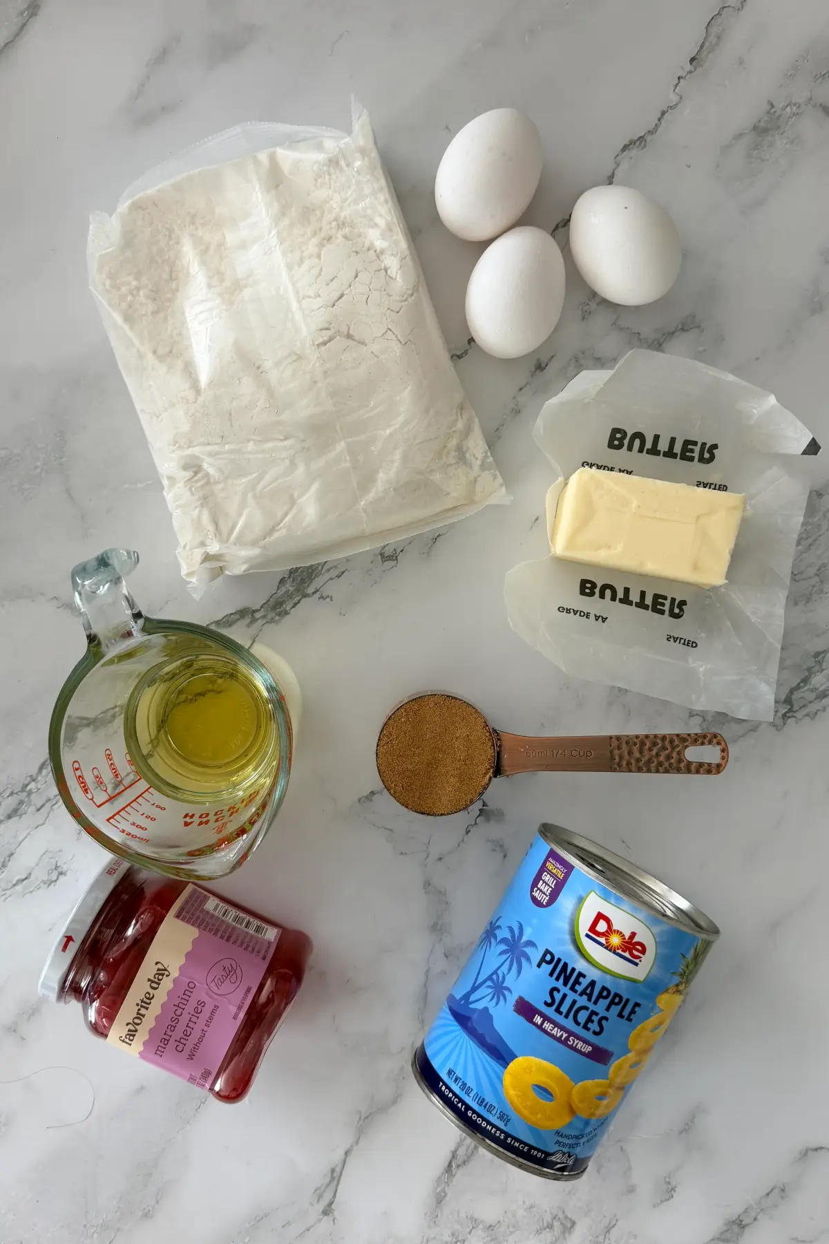 Ingredients for pineapple upside down cake including pineapple slices, cherries, cake mix, eggs, butter, and oil