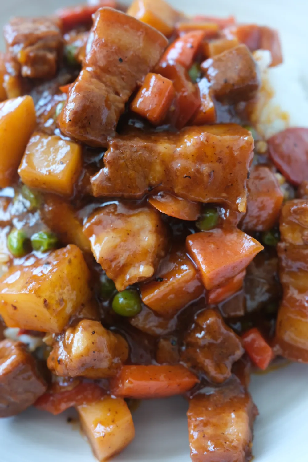 close up of pork menudo served over rice with potatoes, carrots, peas, and hot dogs