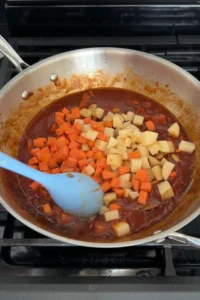 adding diced potatoes and carrots to pork menudo sauce