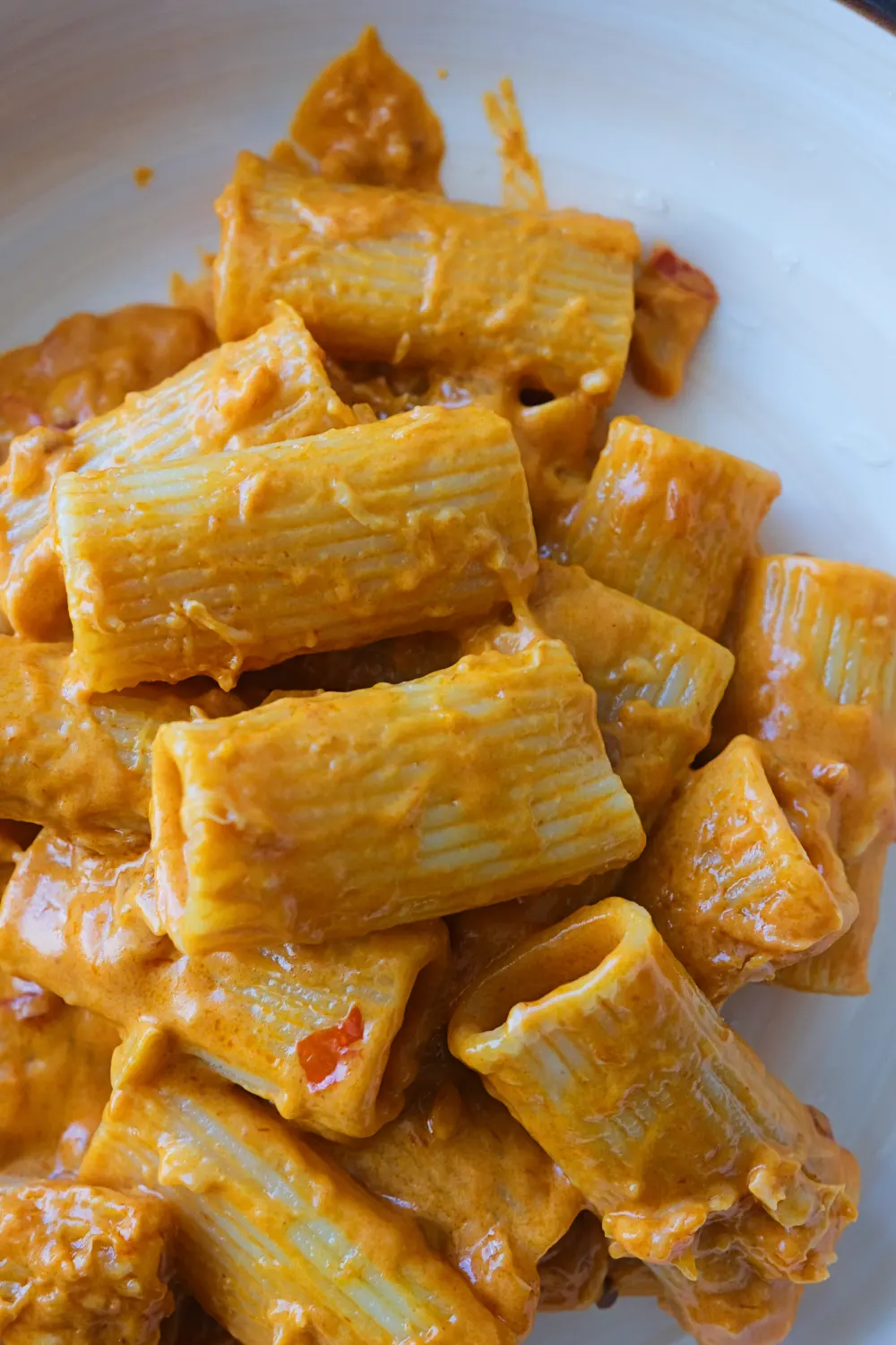 Close-up of spicy rigatoni in a white bowl coated in thick, creamy orange sauce.