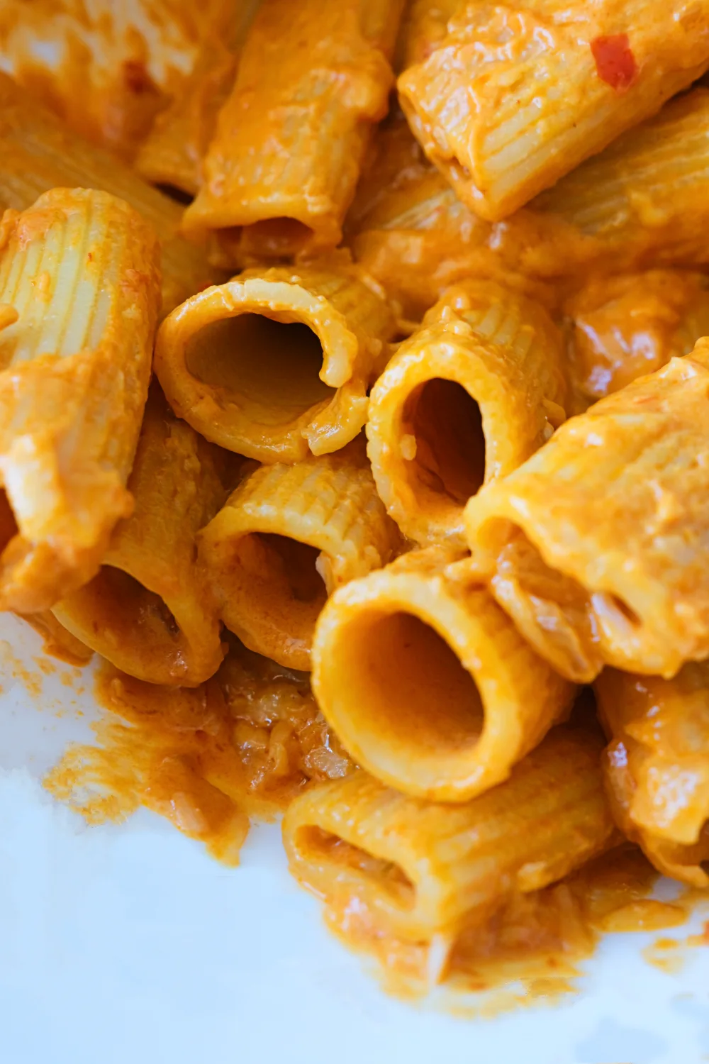 Close-up of spicy rigatoni coated in creamy chili sauce with visible onion and red pepper bits.