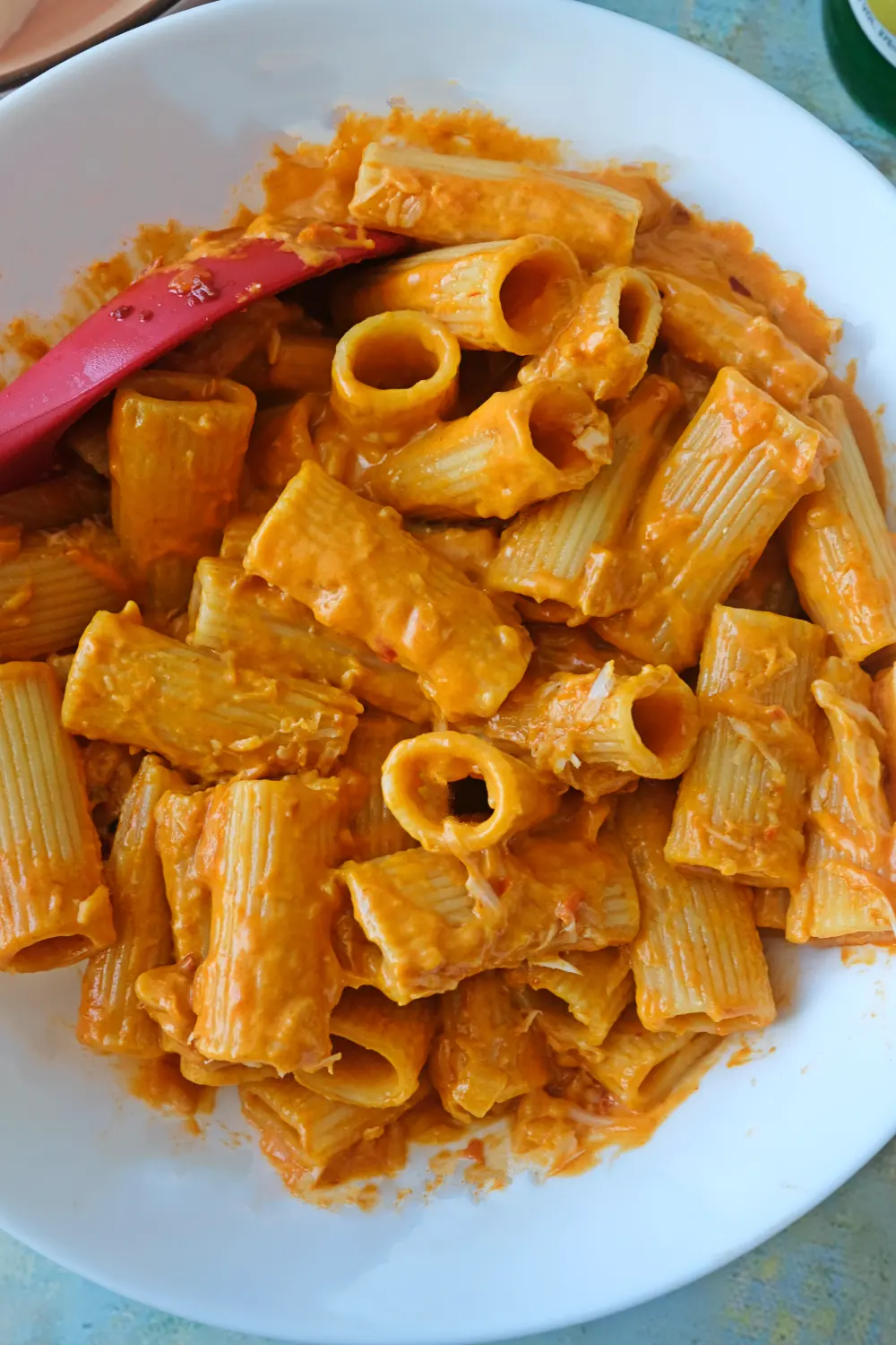 Creamy spicy rigatoni coated in orange-red sauce in a white bowl with a red spoon.