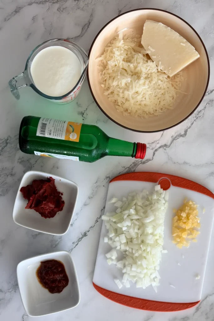 Ingredients for spicy rigatoni arranged on a counter, including heavy cream, pecorino, soju, tomato paste, chili bean sauce, onion, and garlic.