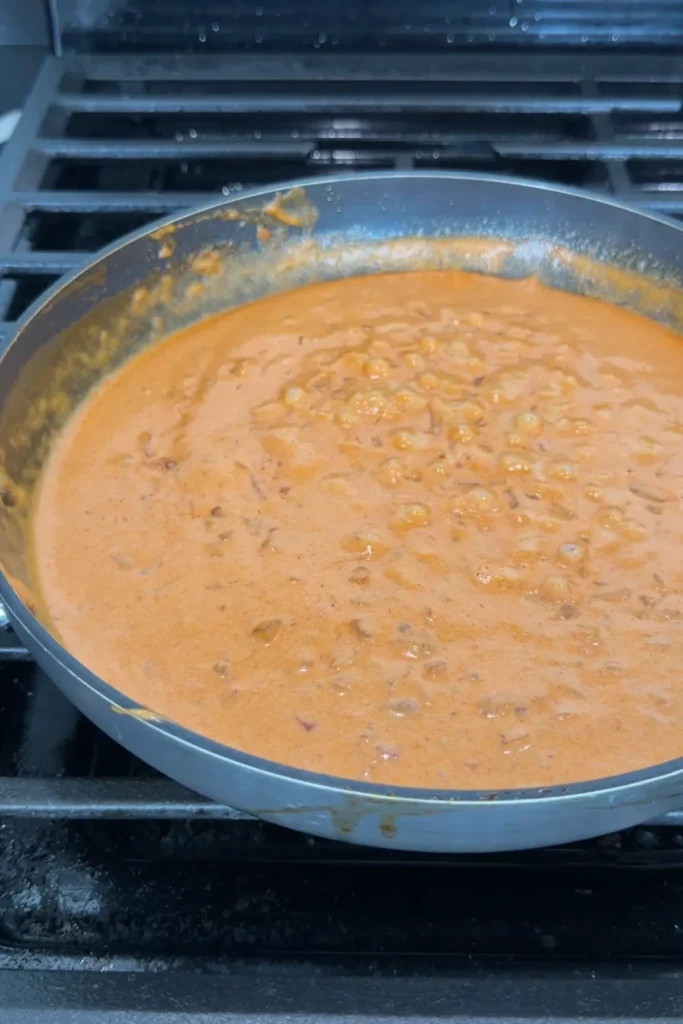 Creamy spicy sauce bubbling gently in a skillet after the heavy cream has been added.