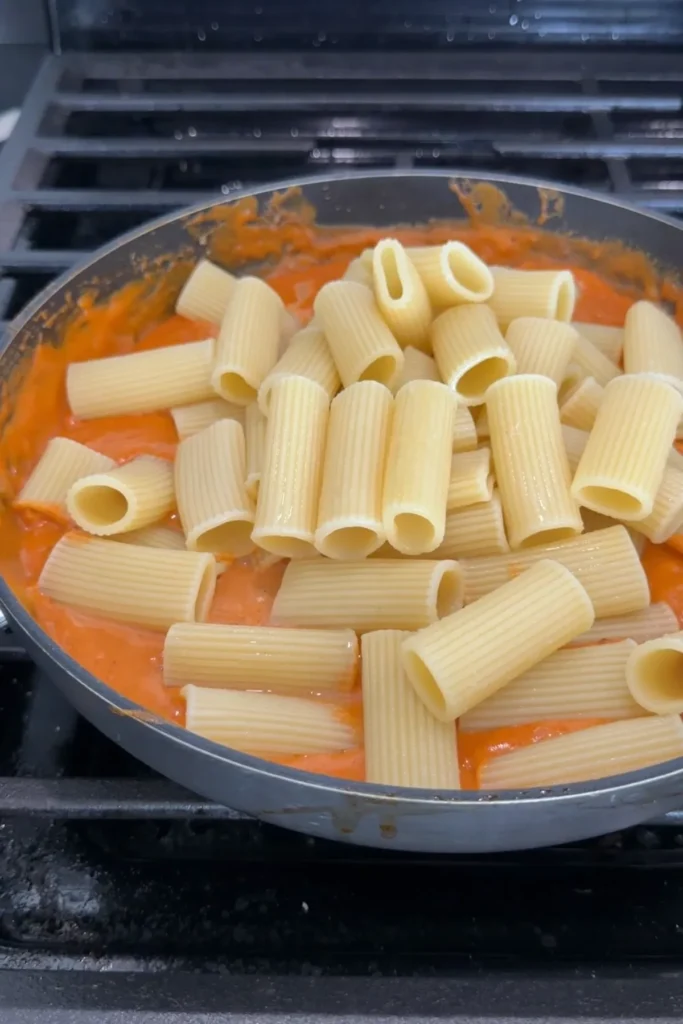Cooked rigatoni added to the creamy spicy sauce in a skillet.