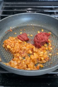 Tomato paste added to softened onion, garlic, and chili bean sauce in a skillet.