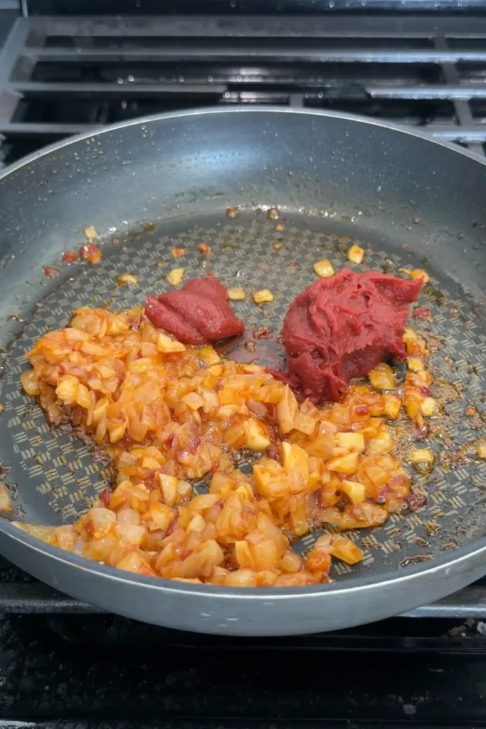 Tomato paste added to softened onion, garlic, and chili bean sauce in a skillet.