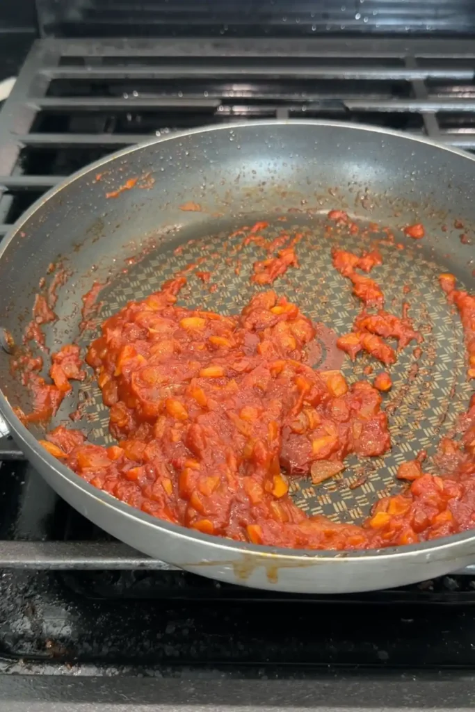 Close-up of the tomato paste mixture cooked until thick, darkened, and concentrated in the skillet.