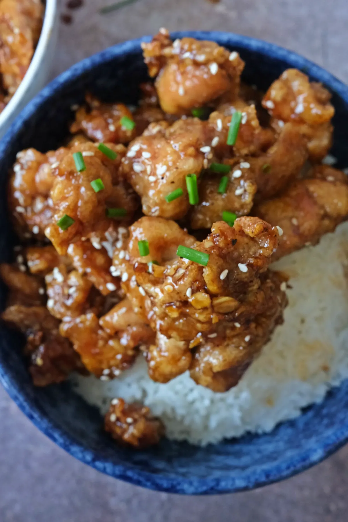 Sticky honey garlic chicken bites served over white rice with sesame seeds and green onions in a blue bowl