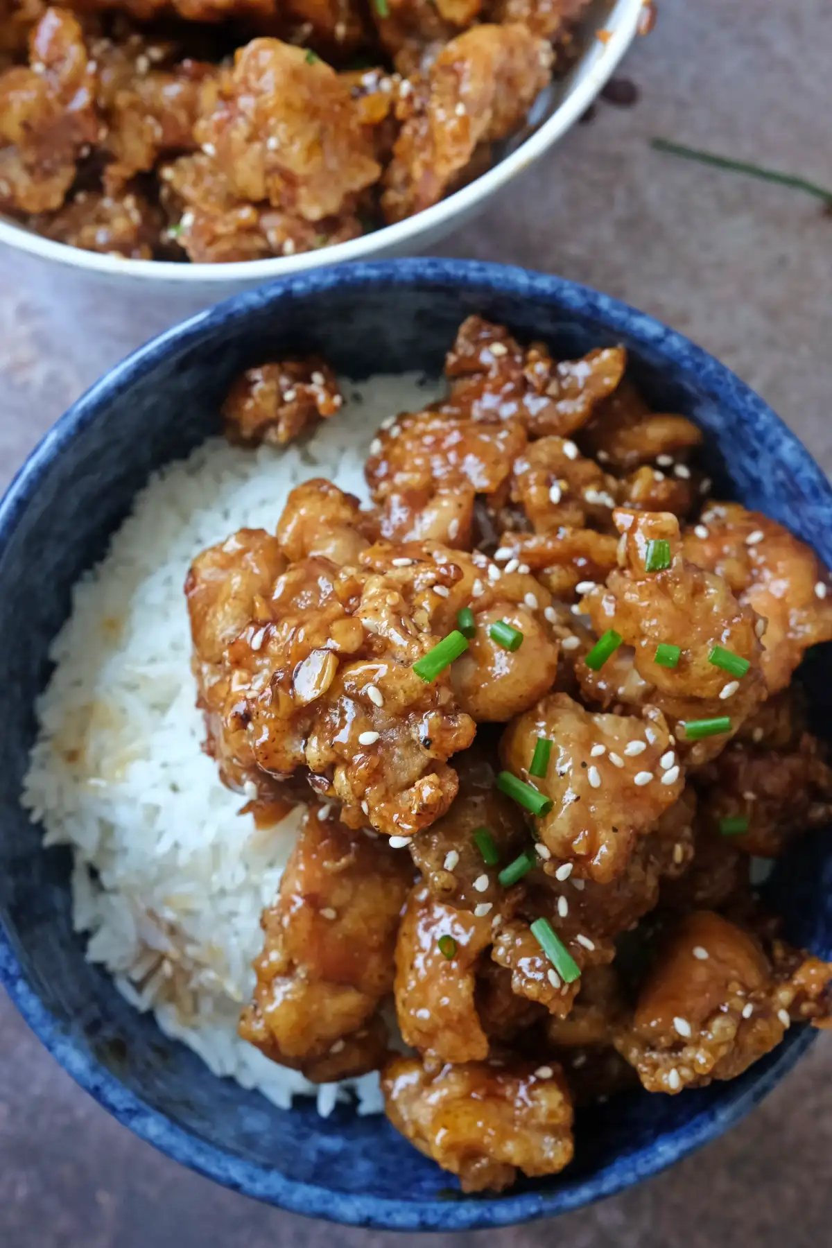 Crispy honey garlic chicken bites glazed in sauce over rice with sesame seeds and chopped chives