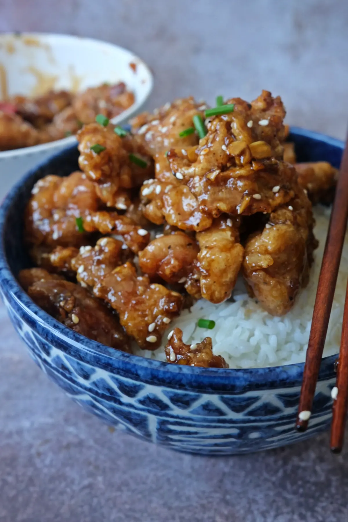 Close-up of sticky honey garlic chicken bites on rice with glossy sauce and chopsticks