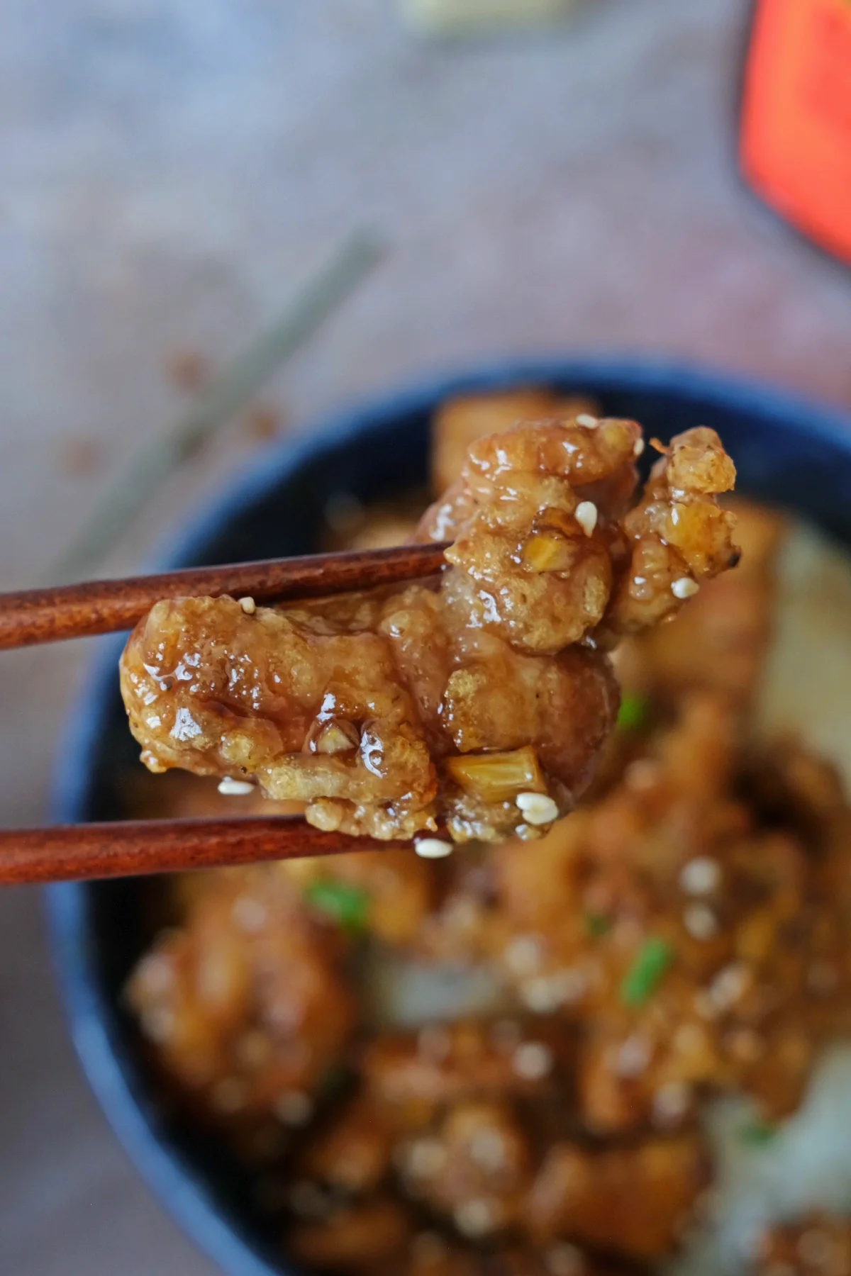 Honey garlic chicken bite held with chopsticks showing crispy coating and sticky glaze