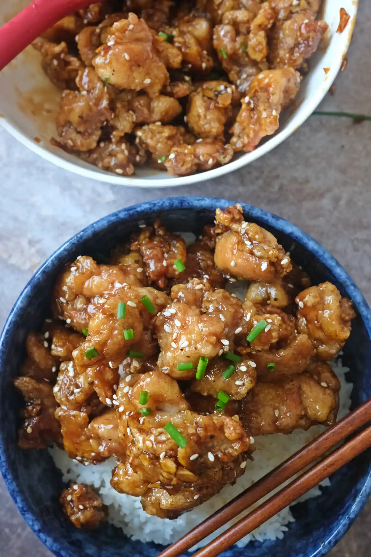 Two bowls of sticky honey garlic chicken bites served over rice with sesame garnish