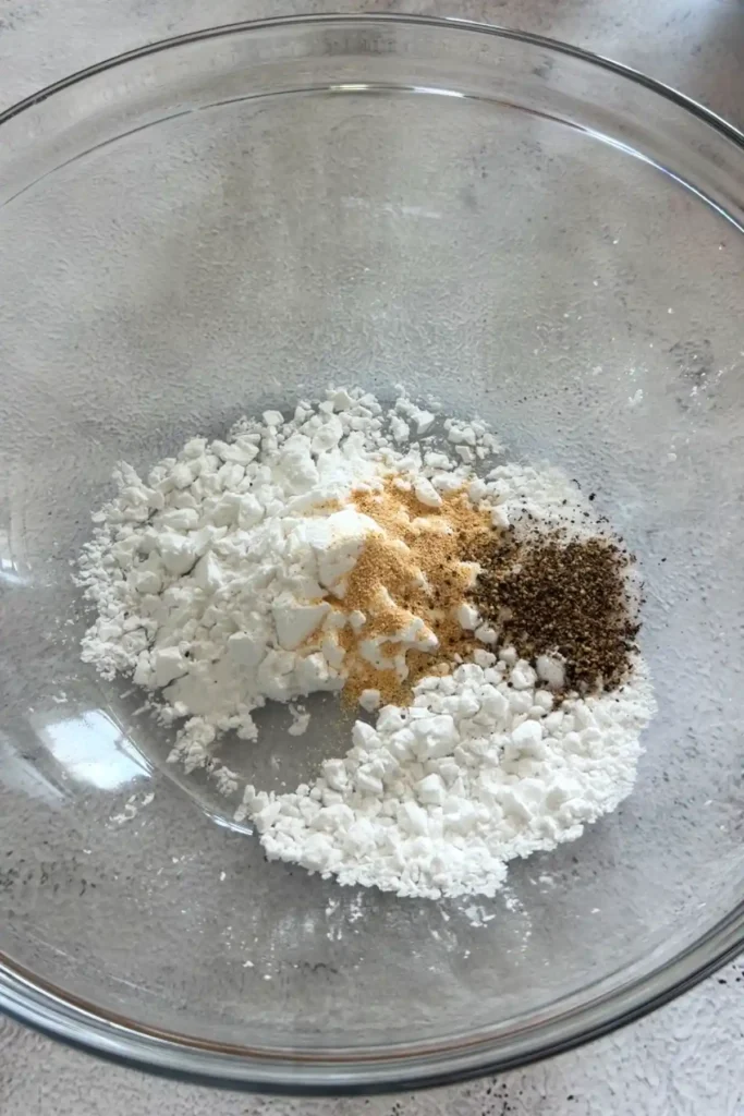 Potato starch, garlic powder, and black pepper in a glass bowl for coating chicken