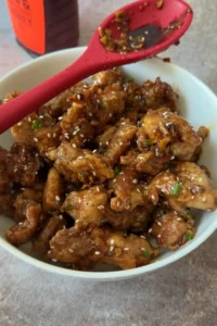 Sticky honey garlic chicken served in a bowl with sesame seeds and green onions
