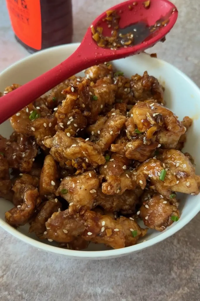 Sticky honey garlic chicken served in a bowl with sesame seeds and green onions