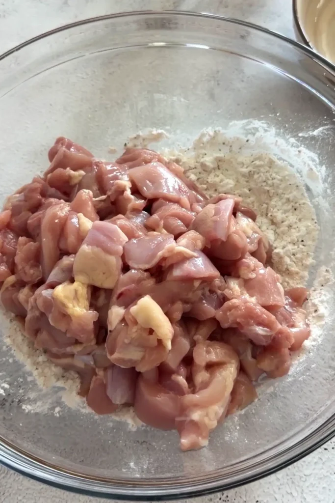 Raw chicken thigh pieces added to seasoned cornstarch mixture
