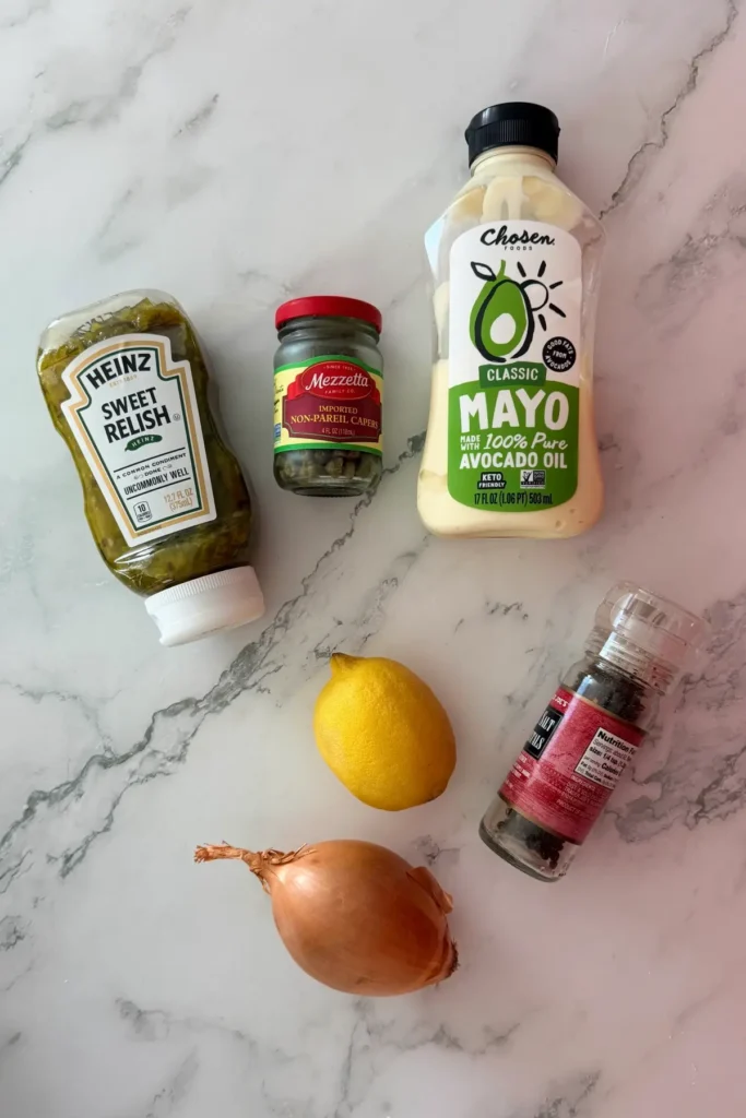 Ingredients for homemade tartar sauce including mayonnaise, capers, relish, lemon, onion, and black pepper.