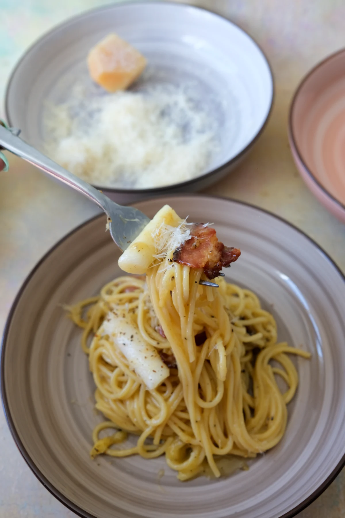 Fork twirling carbonara spaghetti with bacon and a piece of tteokbokki.