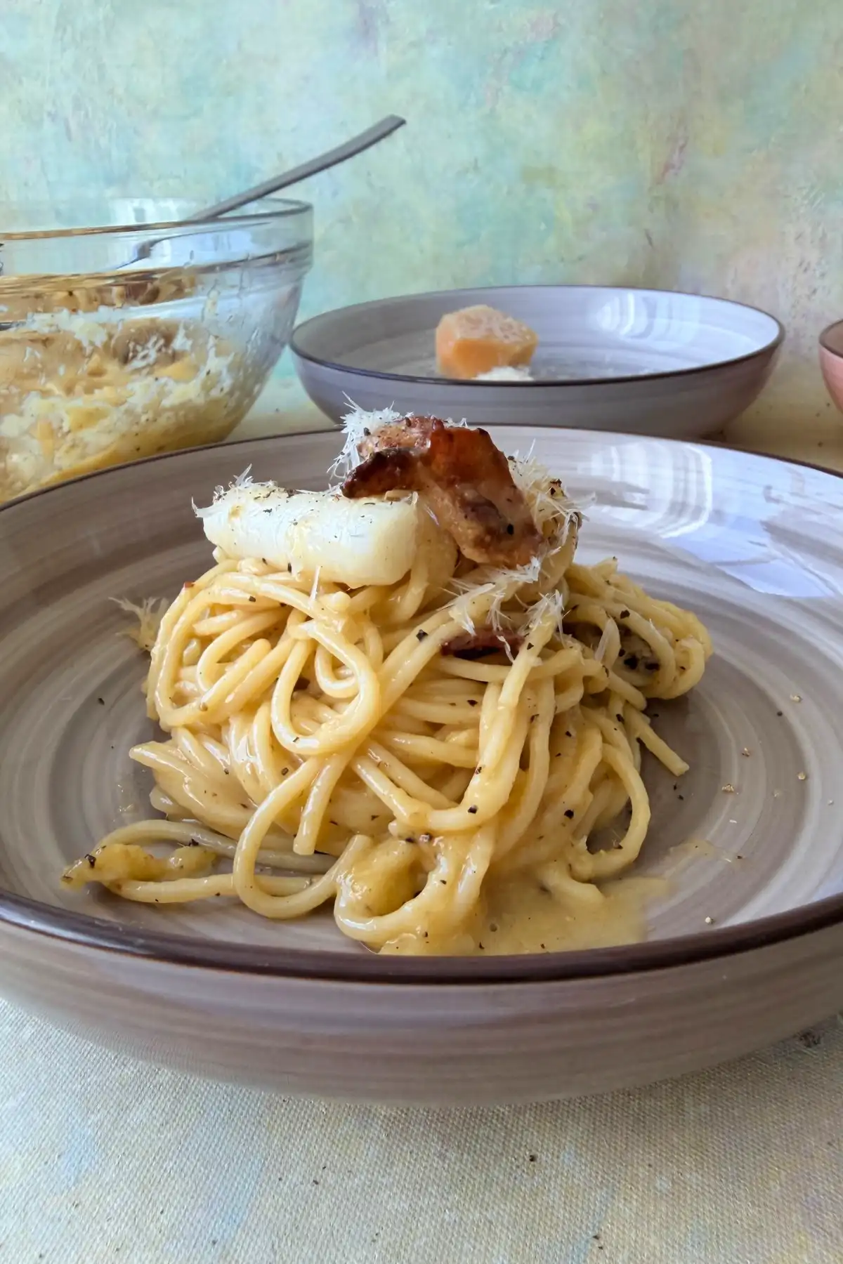 Plated tteokbokki carbonara topped with crispy bacon, Parmesan, and black pepper.