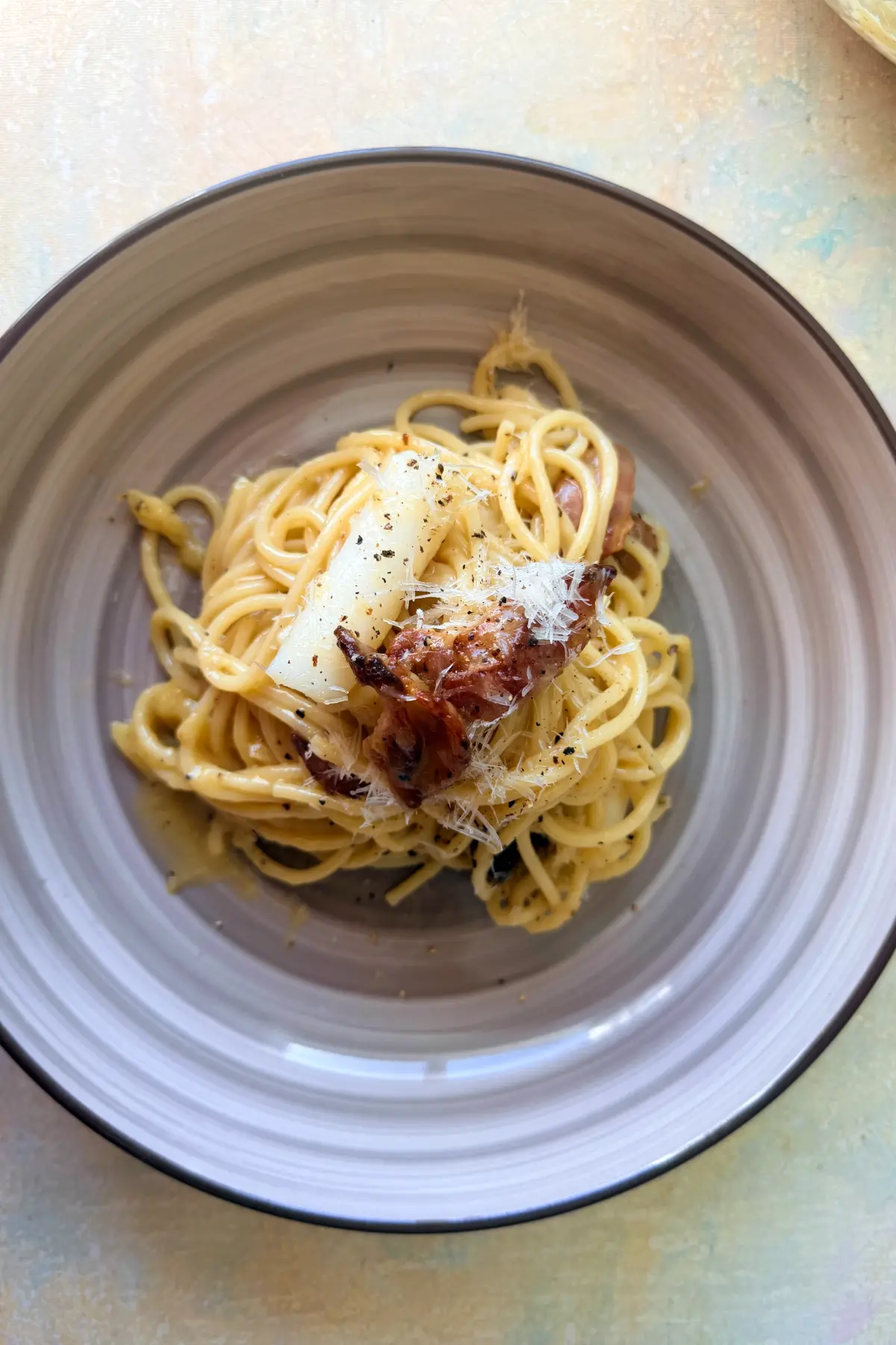 Overhead view of plated tteokbokki carbonara with bacon and grated Parmesan.