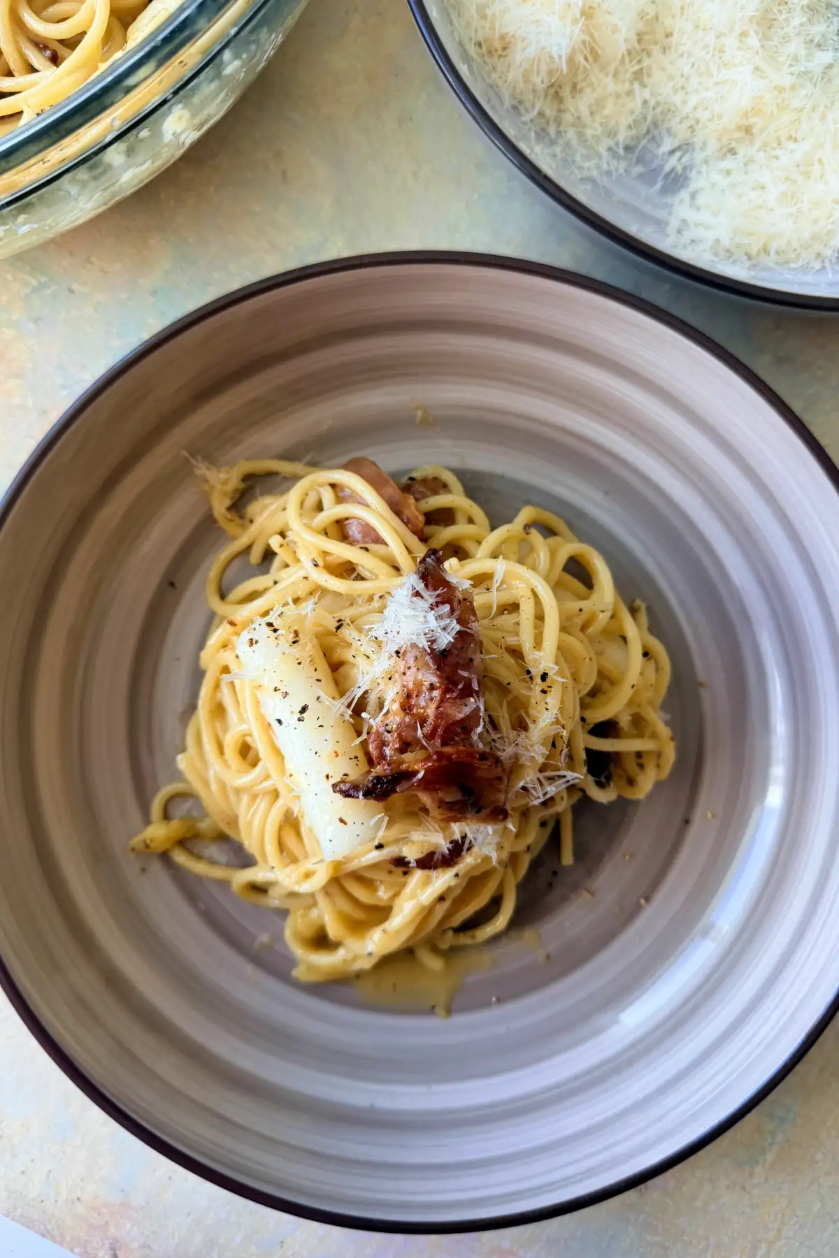 Overhead view of plated tteokbokki carbonara with bacon, grated Parmesan, and black pepper.