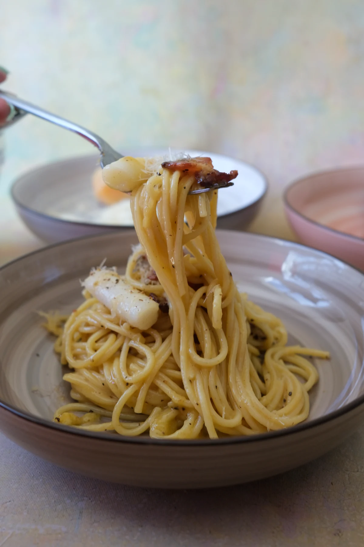 Fork twirling carbonara spaghetti with bacon and a piece of tteokbokki.