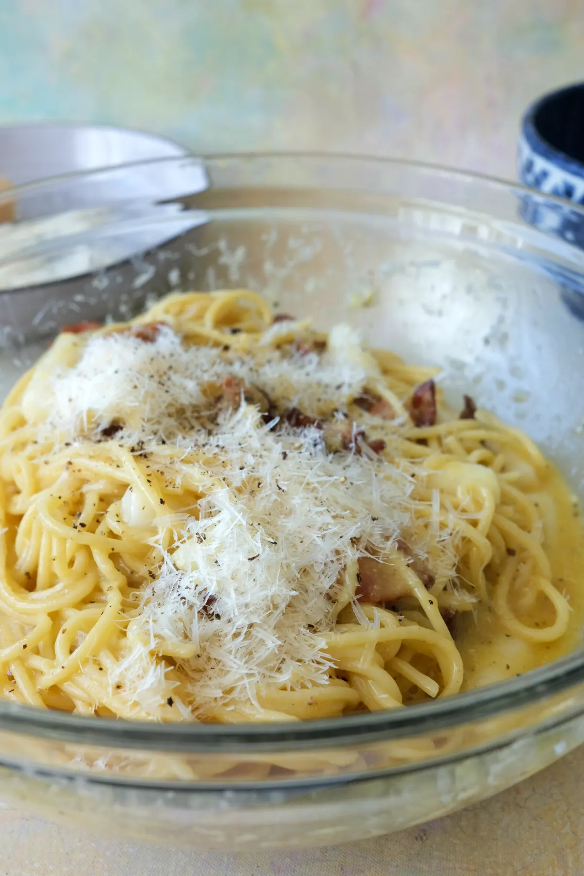 Tteokbokki carbonara tossed with bacon, Parmesan, and black pepper in a glass bowl.