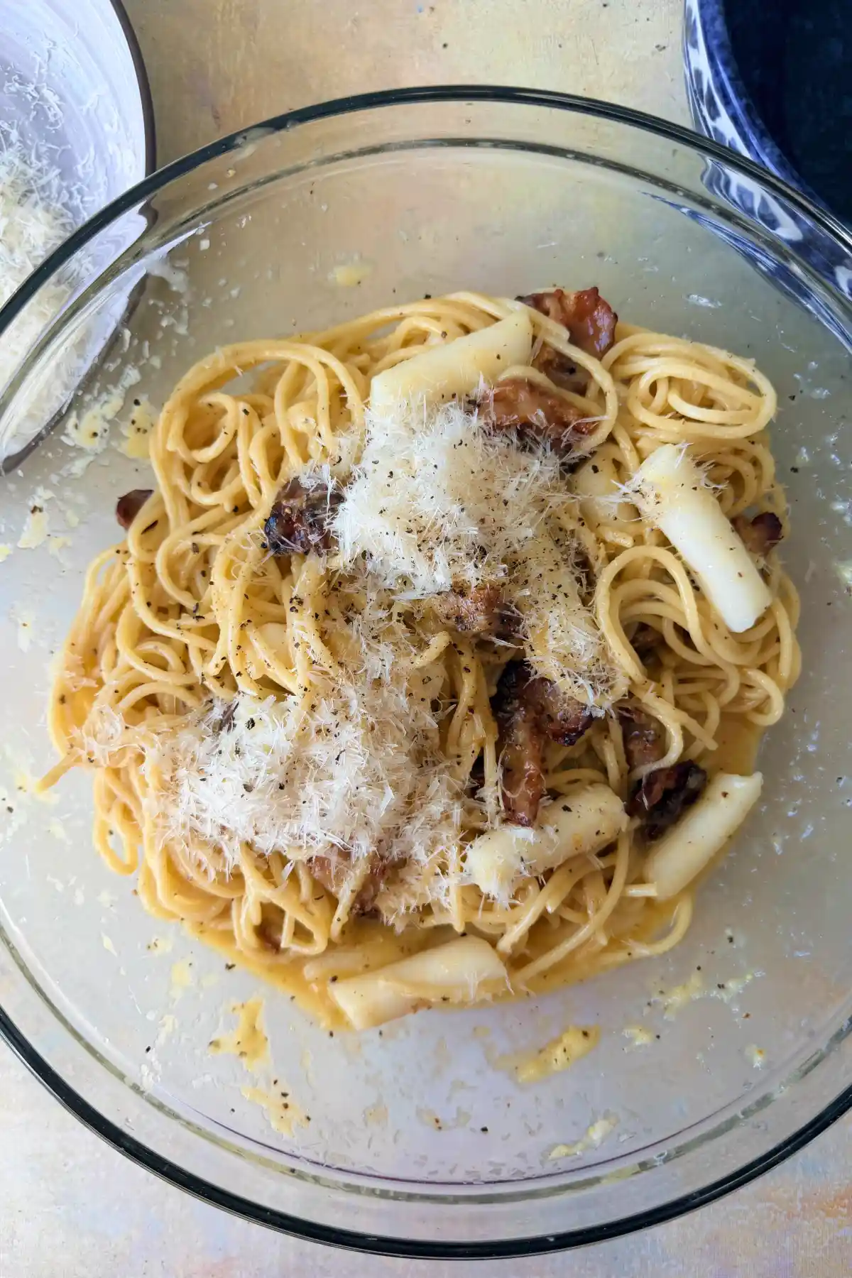 Tteokbokki carbonara tossed with bacon, Parmesan, and black pepper in a glass bowl.