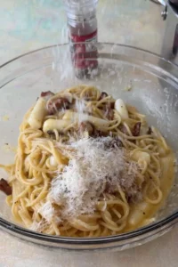 Extra grated Parmesan being added to creamy tteokbokki carbonara in a bowl.