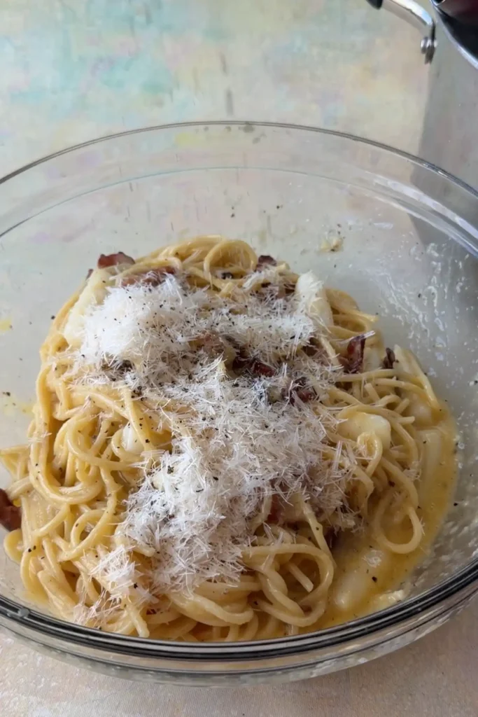 Extra freshly ground pepper being added to creamy tteokbokki carbonara in a bowl.