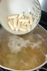 Korean rice cakes being added to boiling pasta water.