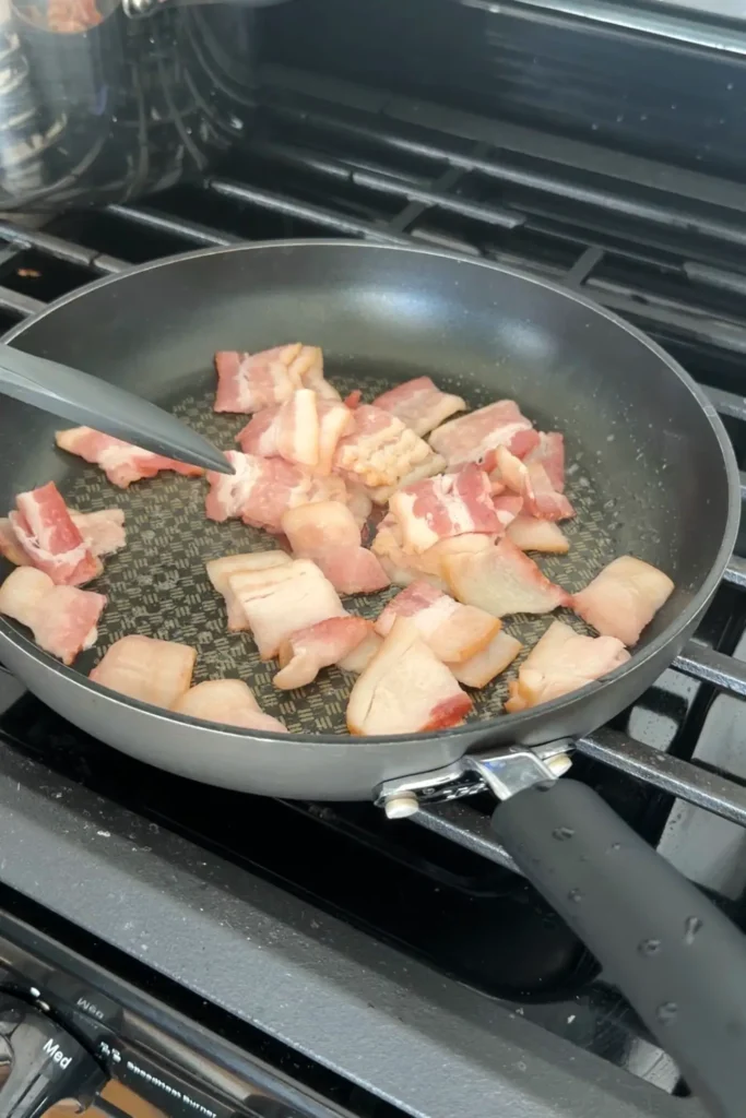 Chopped bacon starting to cook in a skillet.