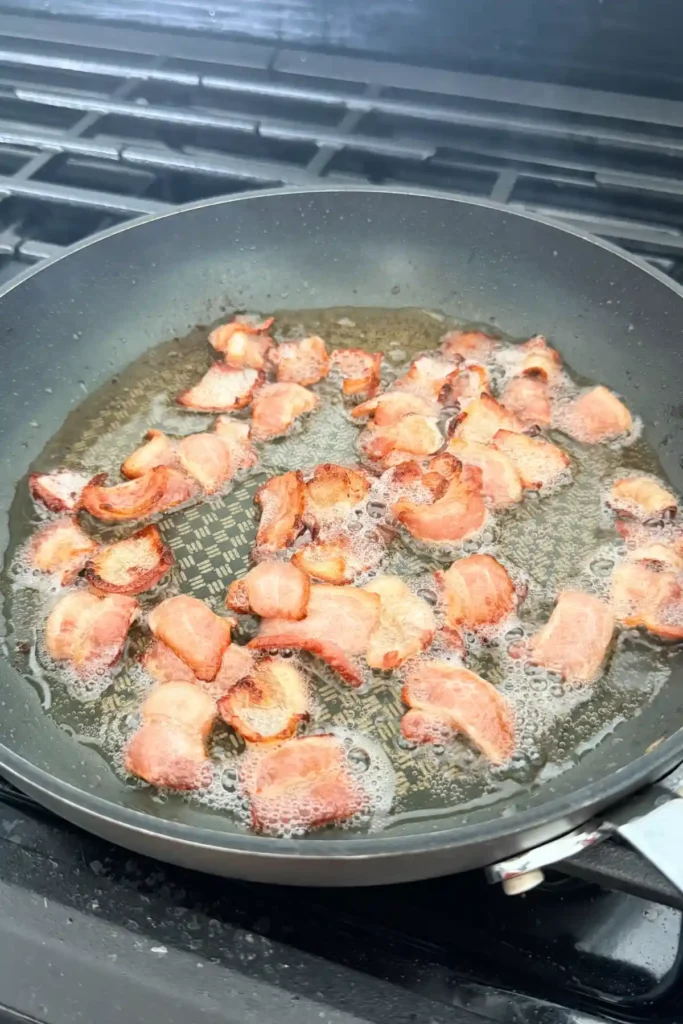 Bacon cooking in a skillet until browned and crispy.