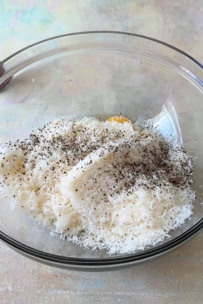 Eggs, Parmesan, and black pepper in a glass bowl before mixing.