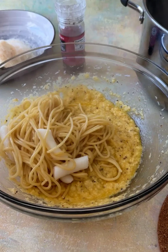 Cooked spaghetti and tteokbokki added to the carbonara mixture in a bowl.