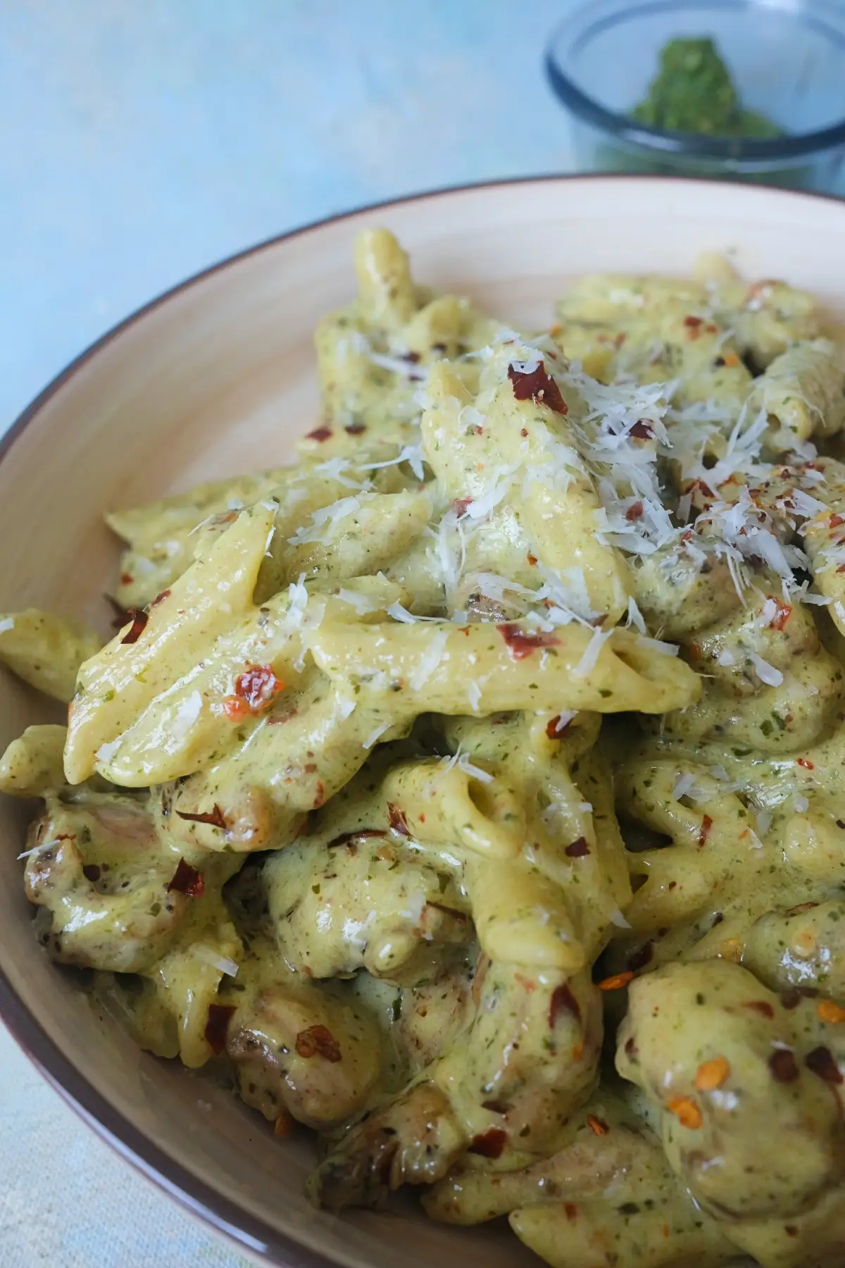 Close-up of almond pesto chicken pasta with penne, creamy basil sauce, parmesan shavings, and chili flakes, showing the thick, glossy texture of the sauce.
