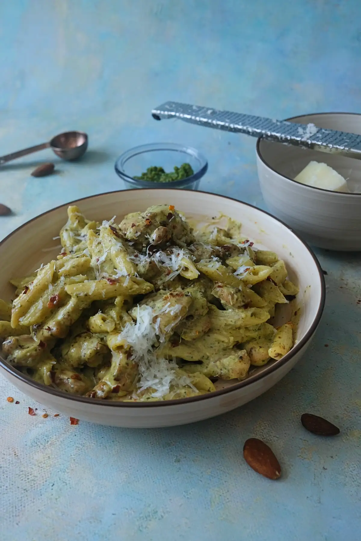 Plated almond pesto pasta with chicken and penne, topped with parmesan and fresh basil
