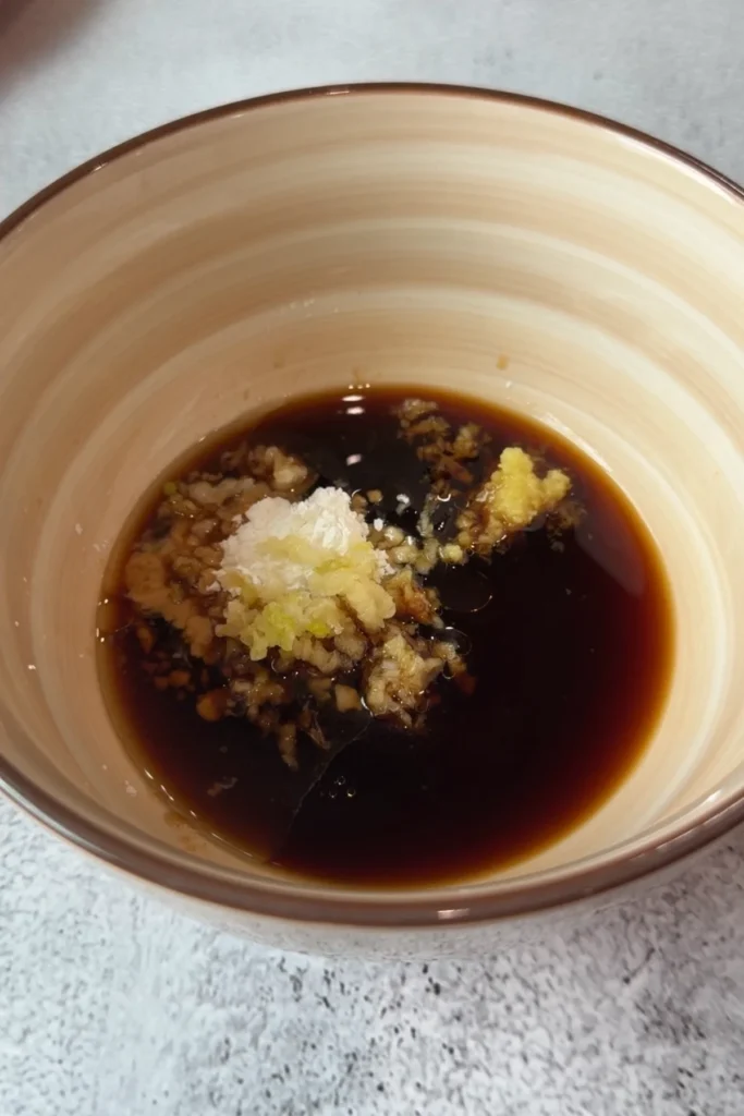 Soy sauce, oyster sauce, minced garlic, minced ginger, sesame oil, and cornstarch added to a beige bowl before whisking the beef and broccoli sauce.
