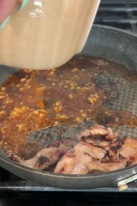 Prepared sauce being poured from a beige bowl into the skillet with browned beef.