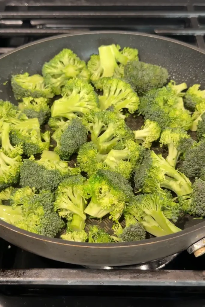 Fresh broccoli florets spread across a nonstick skillet on the stove while cooking until crisp-tender.