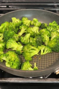 Broccoli florets sautéing in a skillet, starting to turn bright green as they cook.