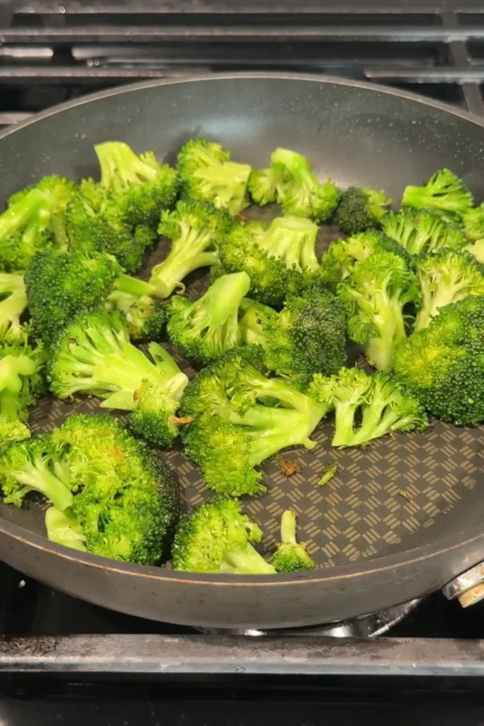 Broccoli florets sautéing in a skillet, starting to turn bright green as they cook.