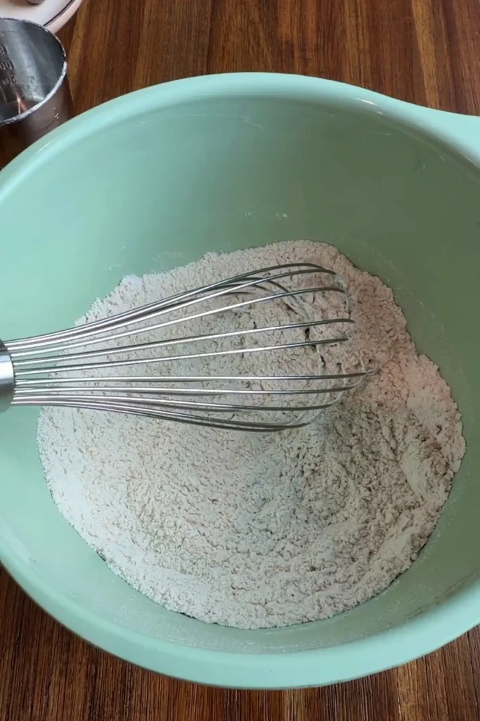 A metal whisk resting in a bowl of flour and spices as the dry ingredients are combined for carrot cupcake batter.
