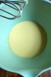 Smooth pale wet mixture in a light green bowl after the eggs, oil, sugar, and vanilla have been whisked until blended.